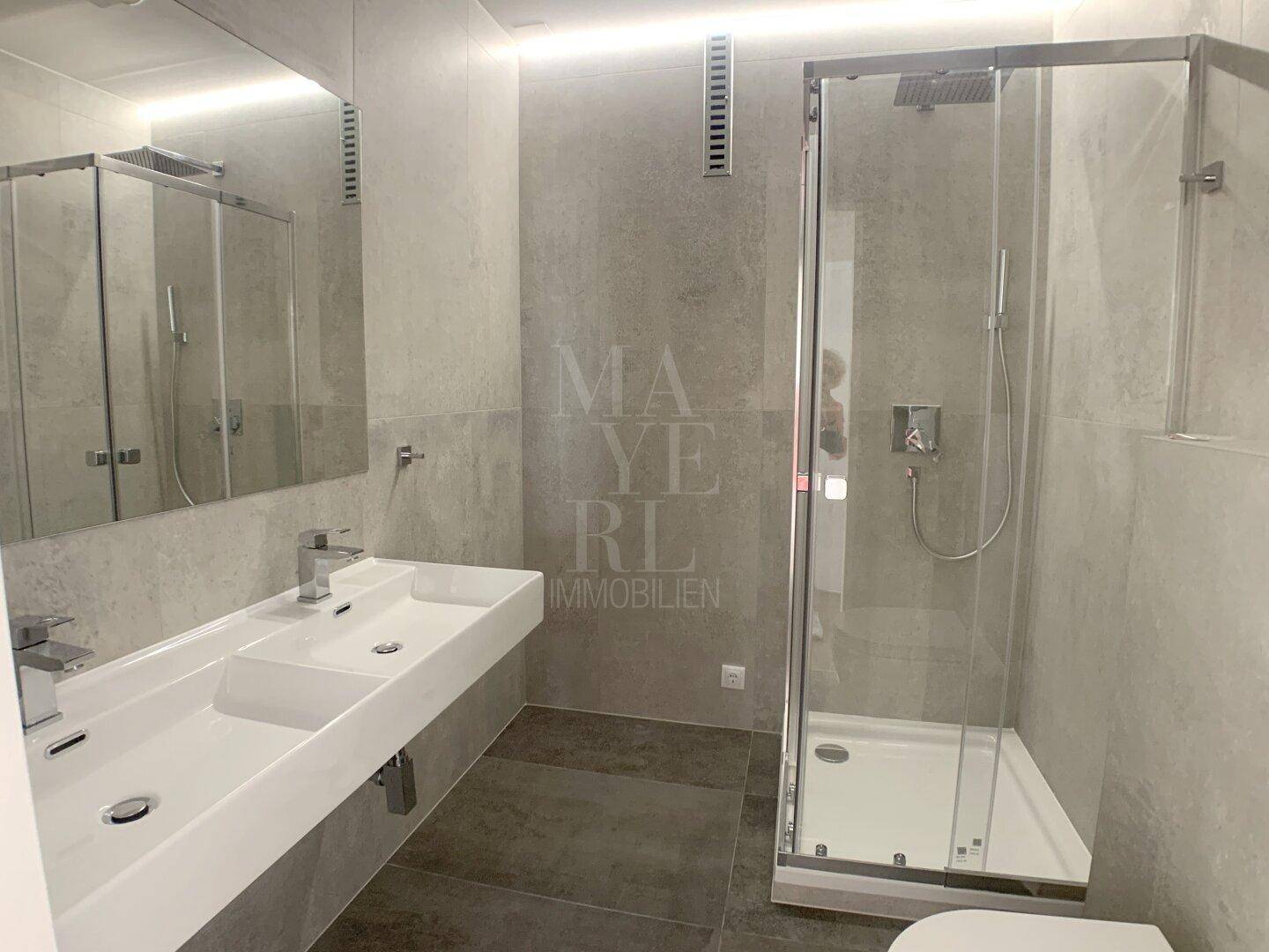 Modernes Badezimmer mit Doppelwaschbecken, Dusche und integrierter Deckenbeleuchtung.