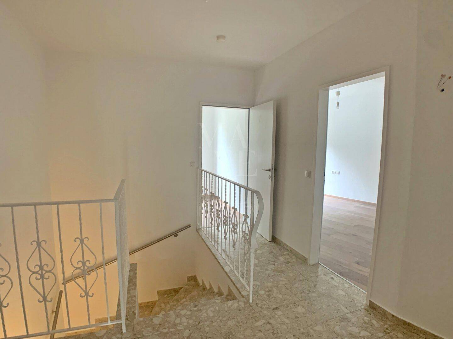 Heller Flur mit Treppe, dekorativem Geländer und Fliesenboden.