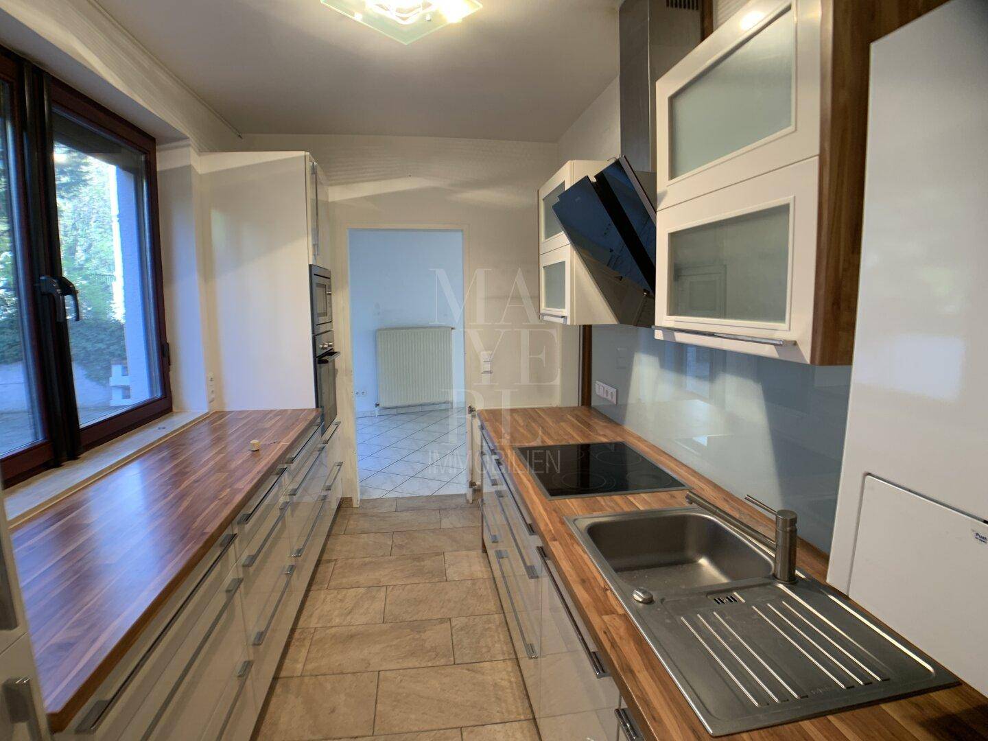 Gut ausgestattete Küche mit Spüle, Induktionskochfeld, Dunstabzugshaube und viel Stauraum.