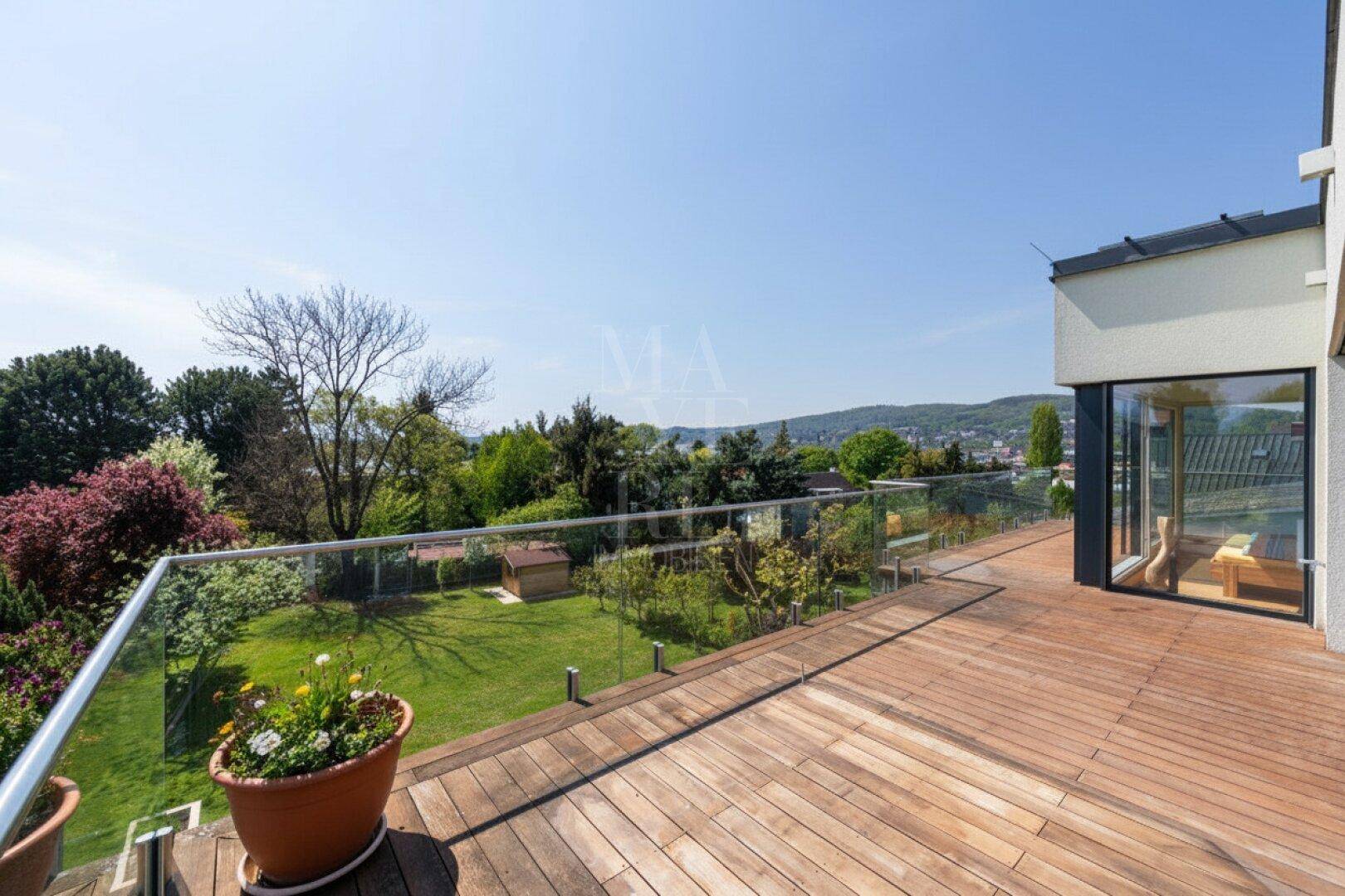 Große Holzterrasse mit Glasgeländer und weitem Blick über den Garten und die umliegende Landschaft.