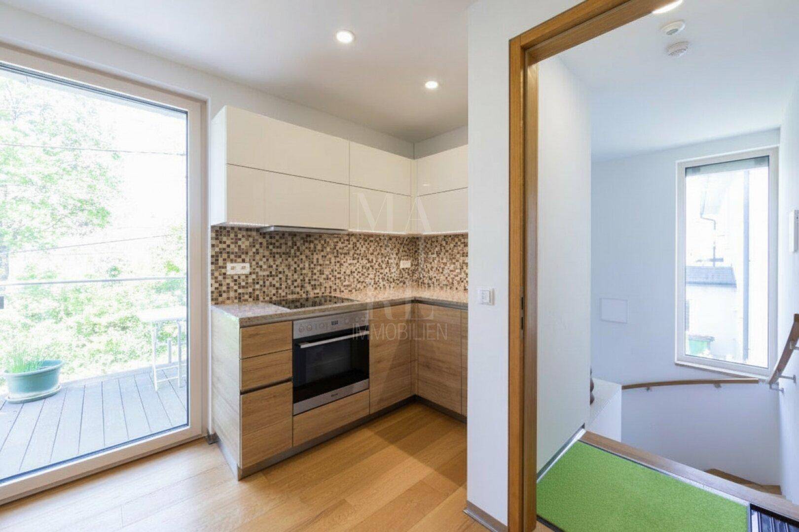 Kompakte Einbauküche mit modernen Holzfronten, Mosaikfliesen und Zugang zu einem Balkon.