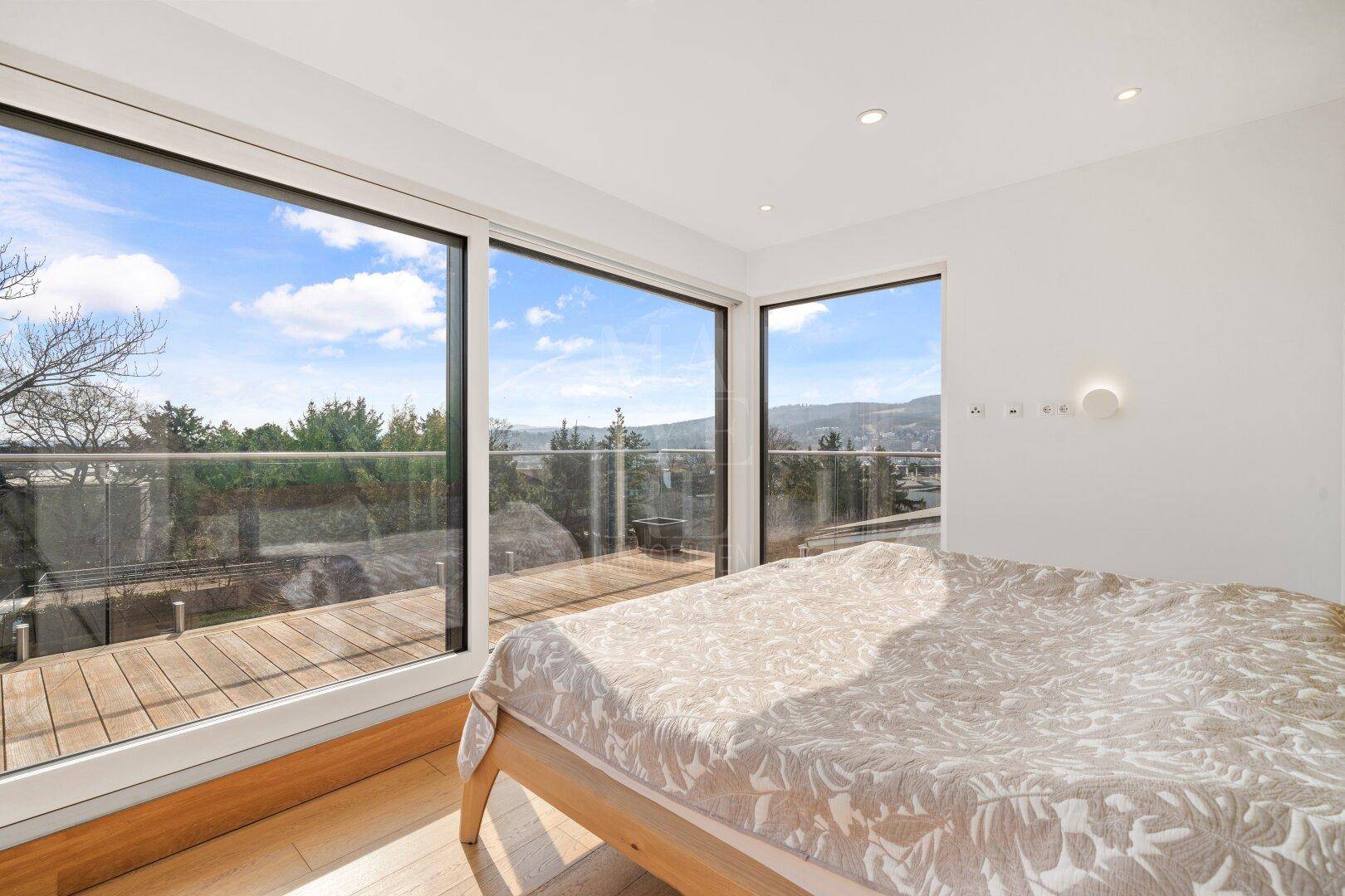 Schlafzimmer mit großen Panoramafenstern, die Zugang zu einer Holzterrasse und weitem Ausblick bieten.