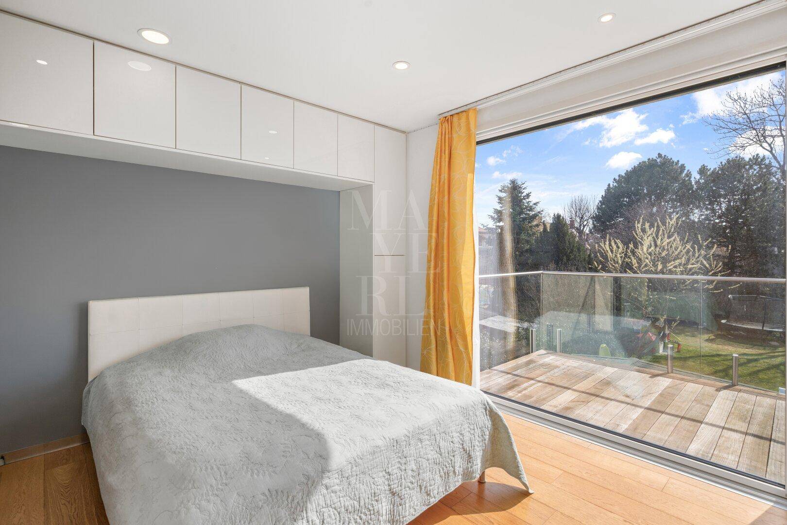 Schlafzimmer mit großen Fenstern, die auf eine Terrasse führen und einen schönen Blick ins Grüne bieten.