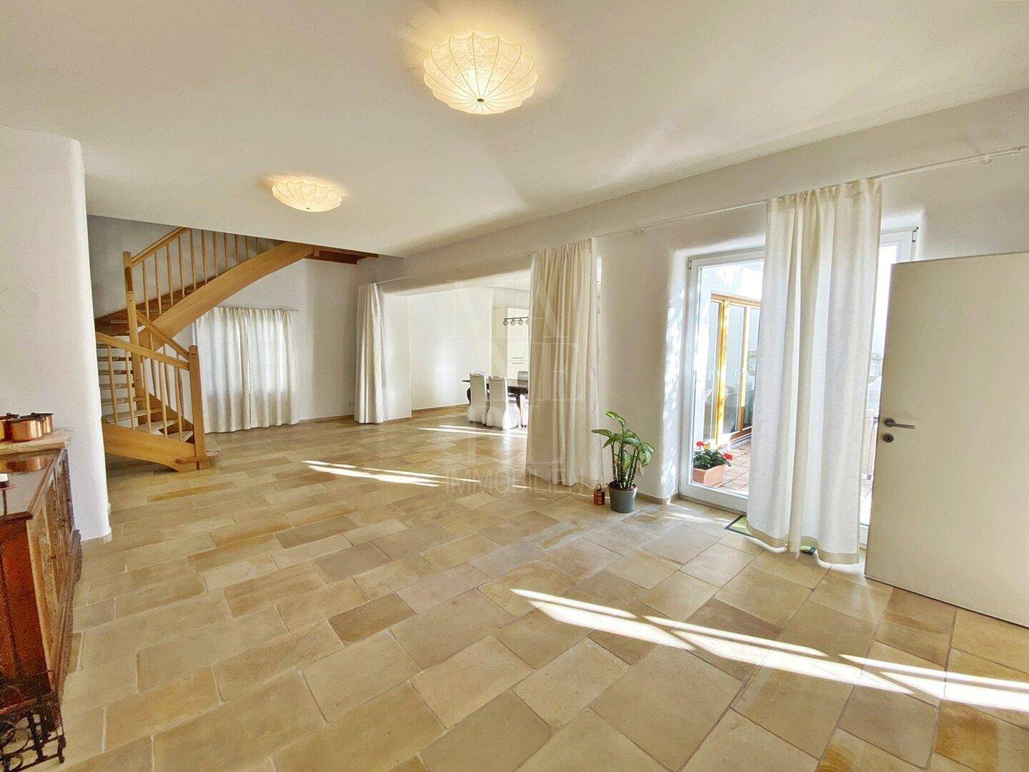 Heller Wohnbereich mit eleganter Holztreppe und großformatigen Fliesen, lichtdurchflutet.