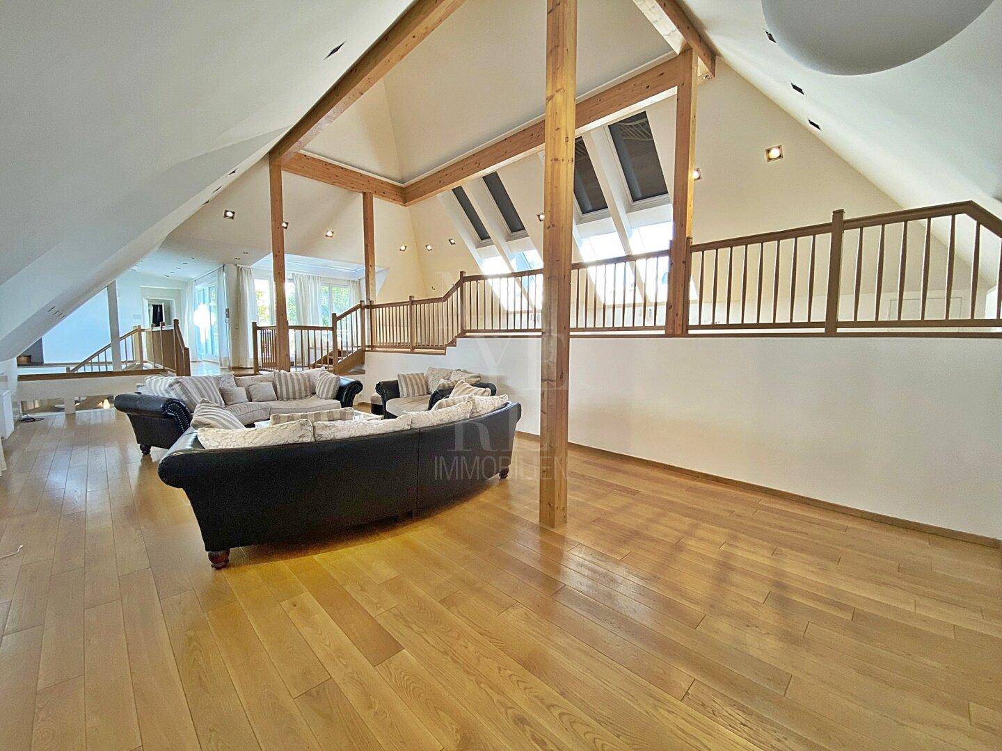 Weitläufiger Wohnbereich mit Holzboden, sichtbaren Holzbalken und viel natürlichem Licht.