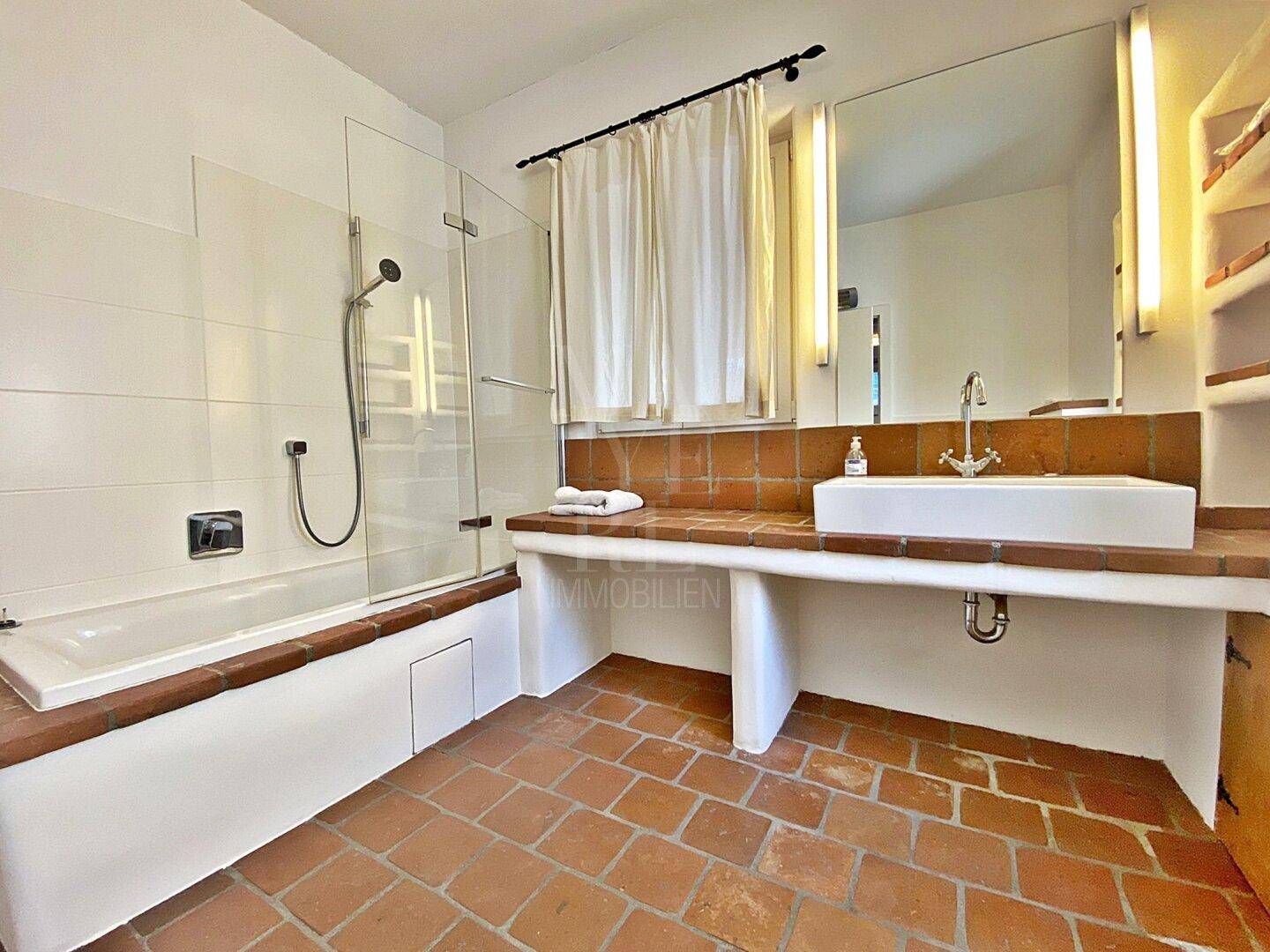 Rustikales Badezimmer mit Terrakotta-Fliesenboden, Badewanne mit Duschfunktion und Waschtisch.