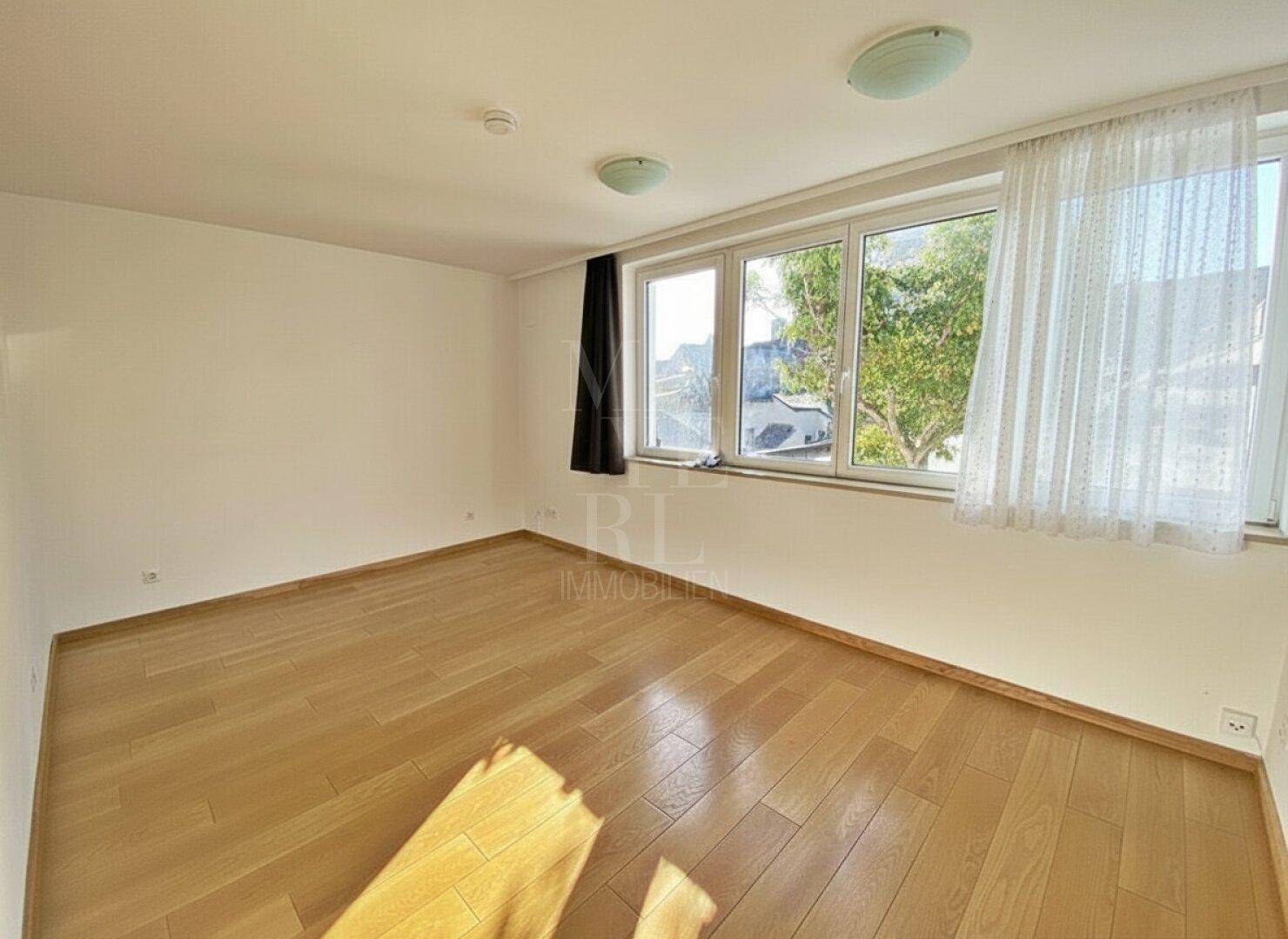 Helles Schlafzimmer mit Holzboden und großen Fenstern, die viel Tageslicht hereinlassen.