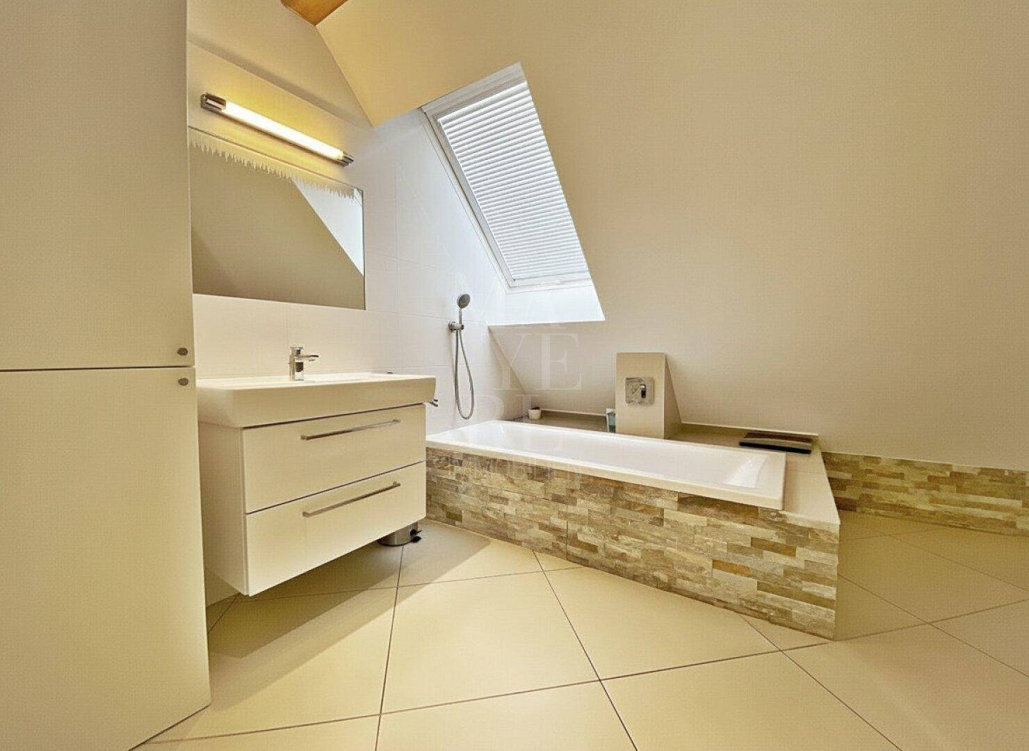 Modernes Badezimmer mit Badewanne, Waschtisch und Dachfenster unter einer Dachschräge.