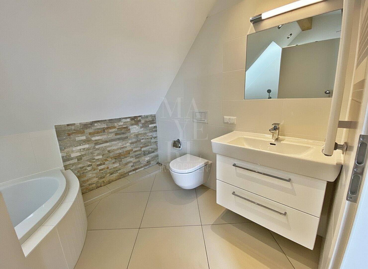 Modernes Badezimmer mit Waschtisch, wandhängendem WC und Badewanne unter Dachschräge.