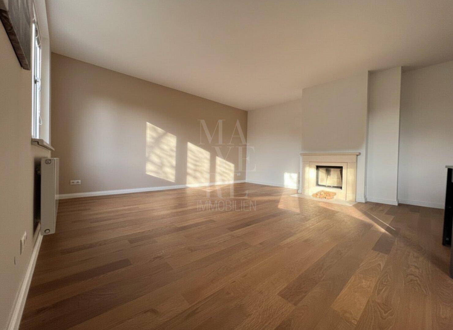 Geräumiger Wohnbereich mit hellem Parkettboden und einem dekorativen Kamin an der Wand.