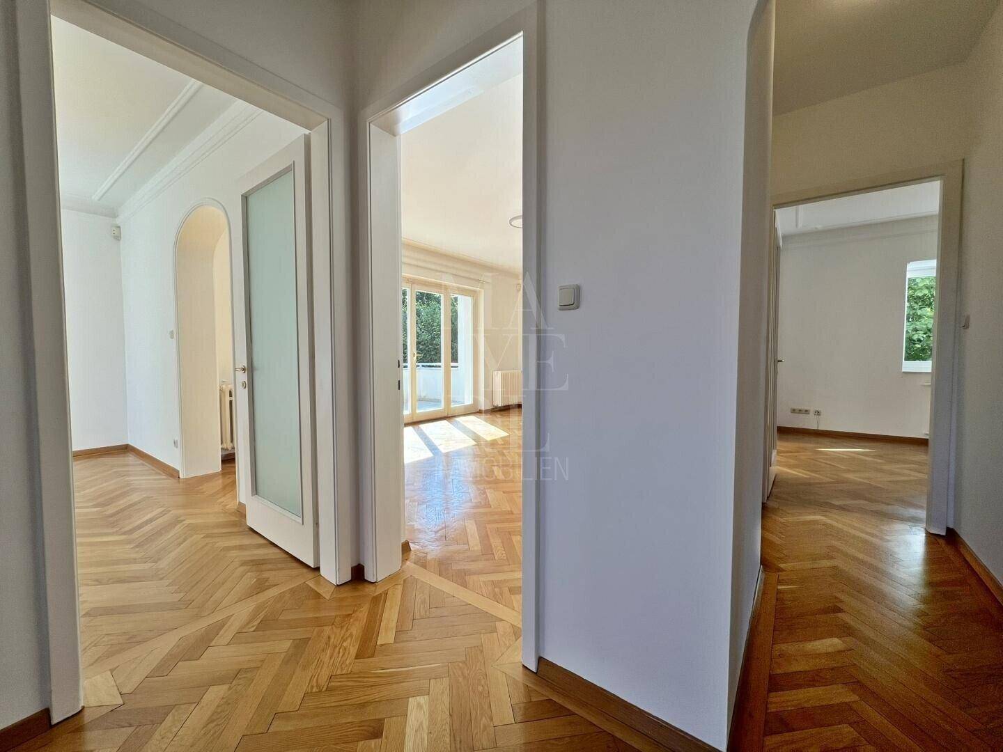 Heller Flur mit elegantem Fischgrätparkett, der zu verschiedenen Räumen führt.