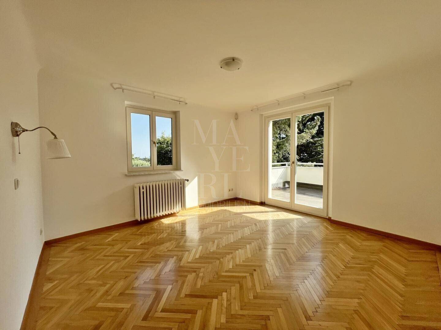 Helles Schlafzimmer mit Fischgrätparkett und Zugang zu einem Balkon oder einer Terrasse.