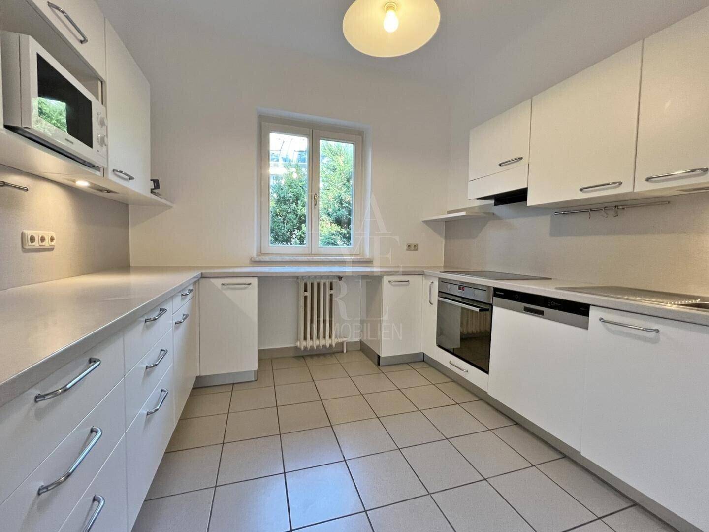 Moderne Einbauküche mit weißen Schränken, hellen Arbeitsplatten und Fliesenboden, gut beleuchtet.
