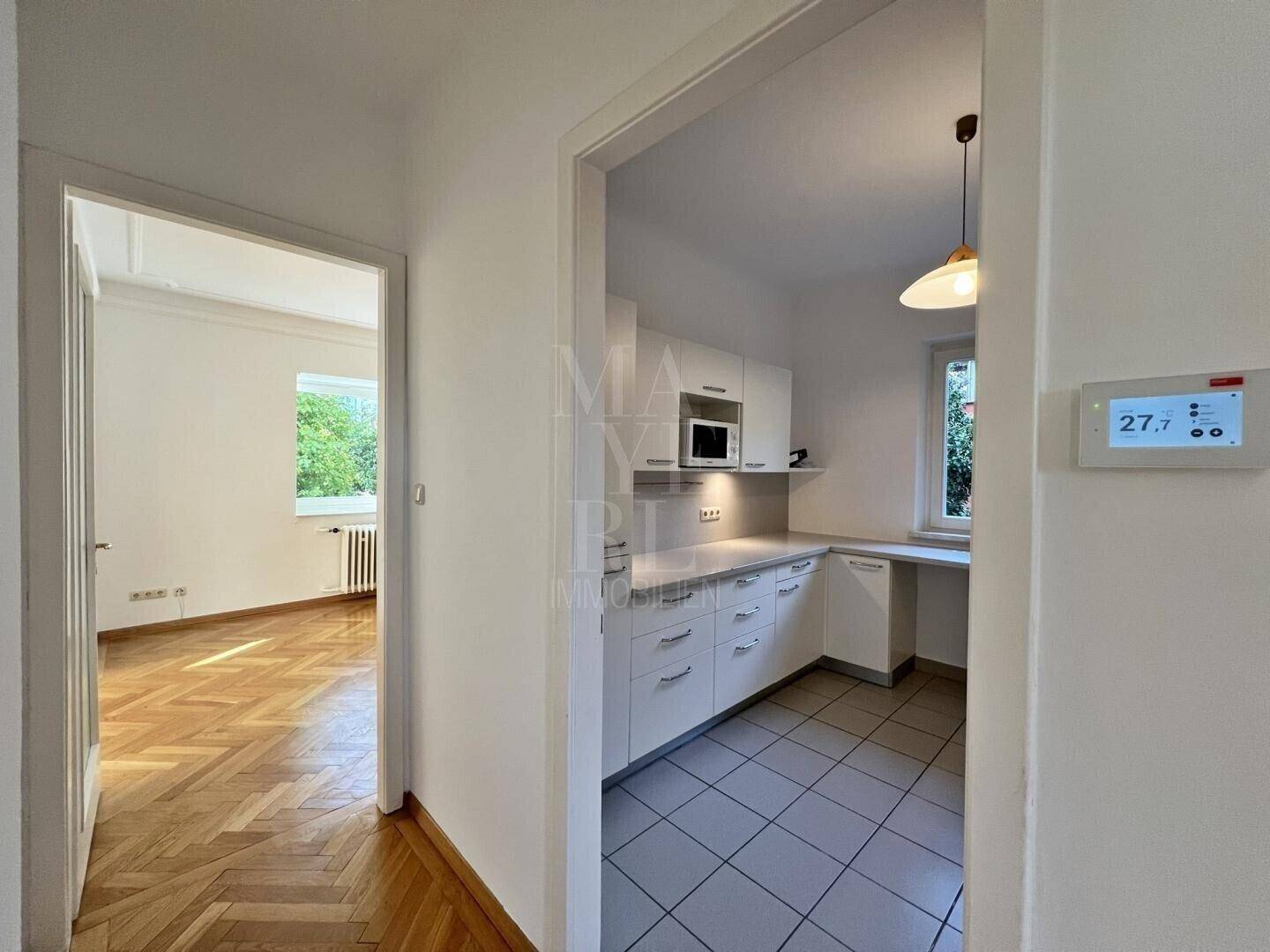 Flur mit Blick in die moderne Küche und einen weiteren Raum mit Parkettboden.
