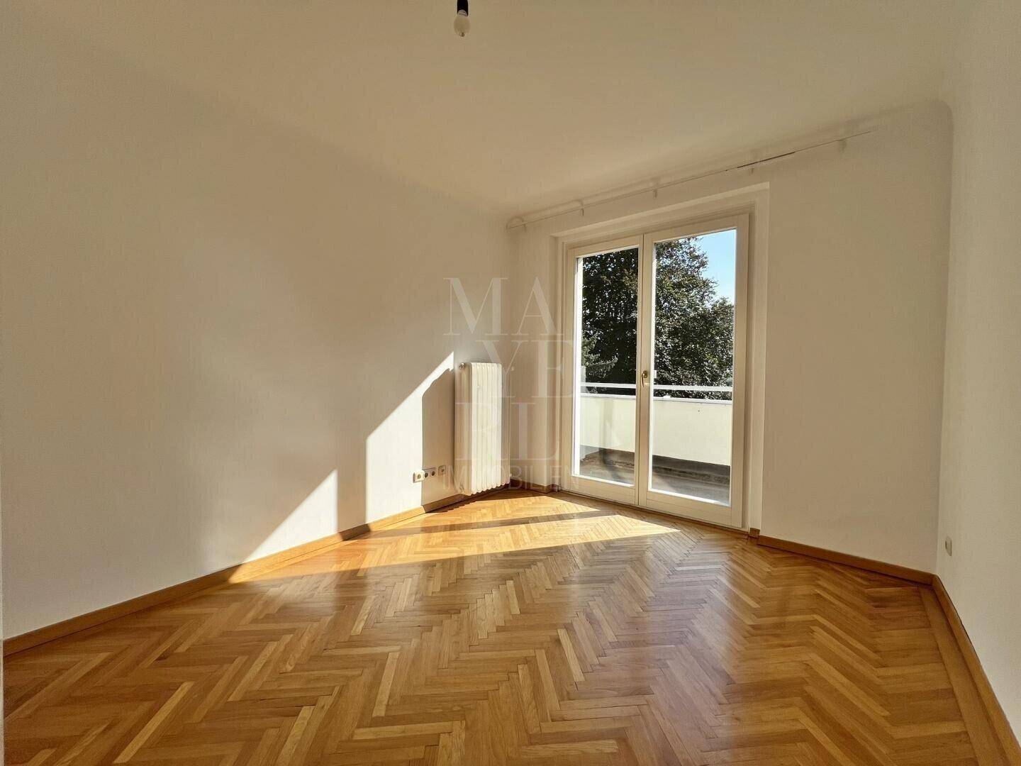 Schlafzimmer mit Fischgrätparkett und direktem Zugang zu einem sonnigen Balkon oder einer Terrasse.