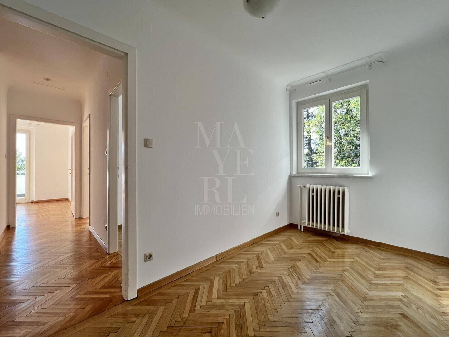 Helles Zimmer mit Fischgrätparkett und einem Fenster, das viel Tageslicht hereinlässt.