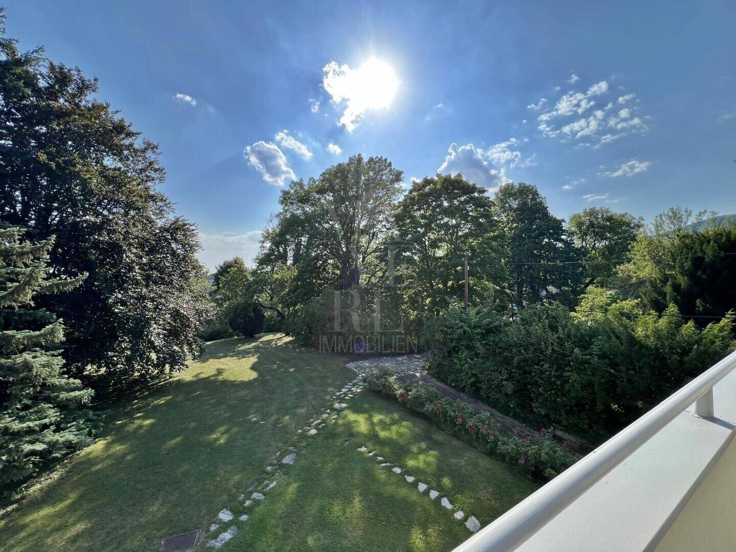 Sonniger Ausblick von der Terrasse auf den weitläufigen Garten mit altem Baumbestand.