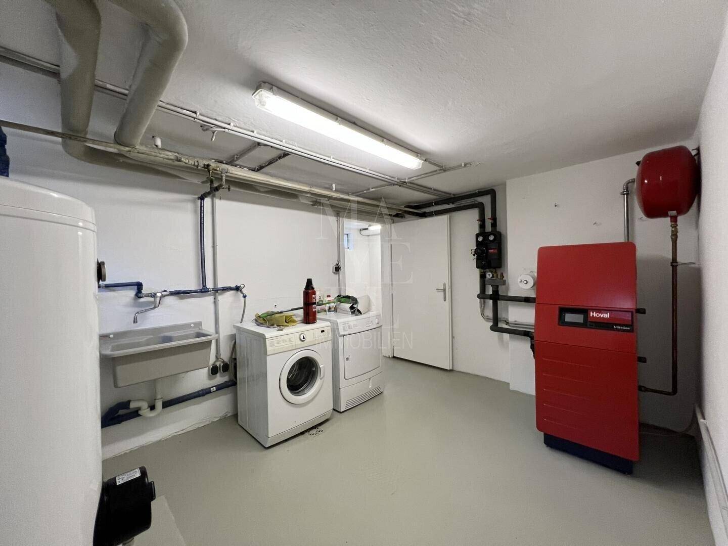 Waschküche im Untergeschoss mit Waschmaschine, Trockner, Spülbecken und Heizungsanlage.
