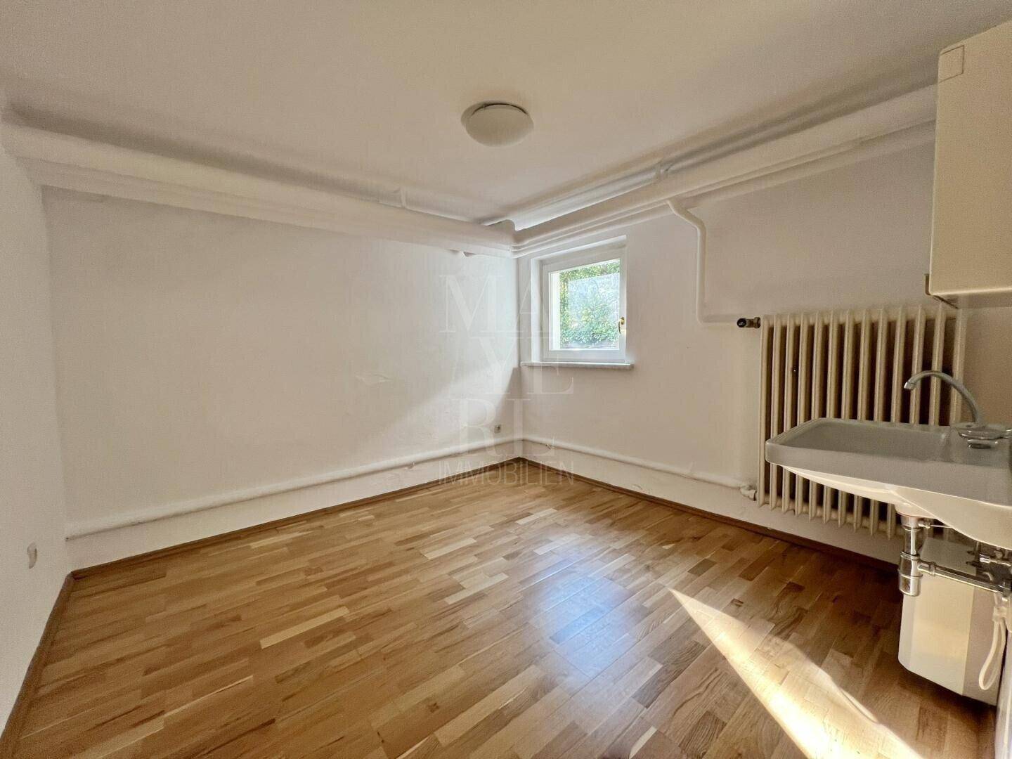 Heller Raum im Untergeschoss mit Holzfußboden, Fenster und einem Waschbecken.