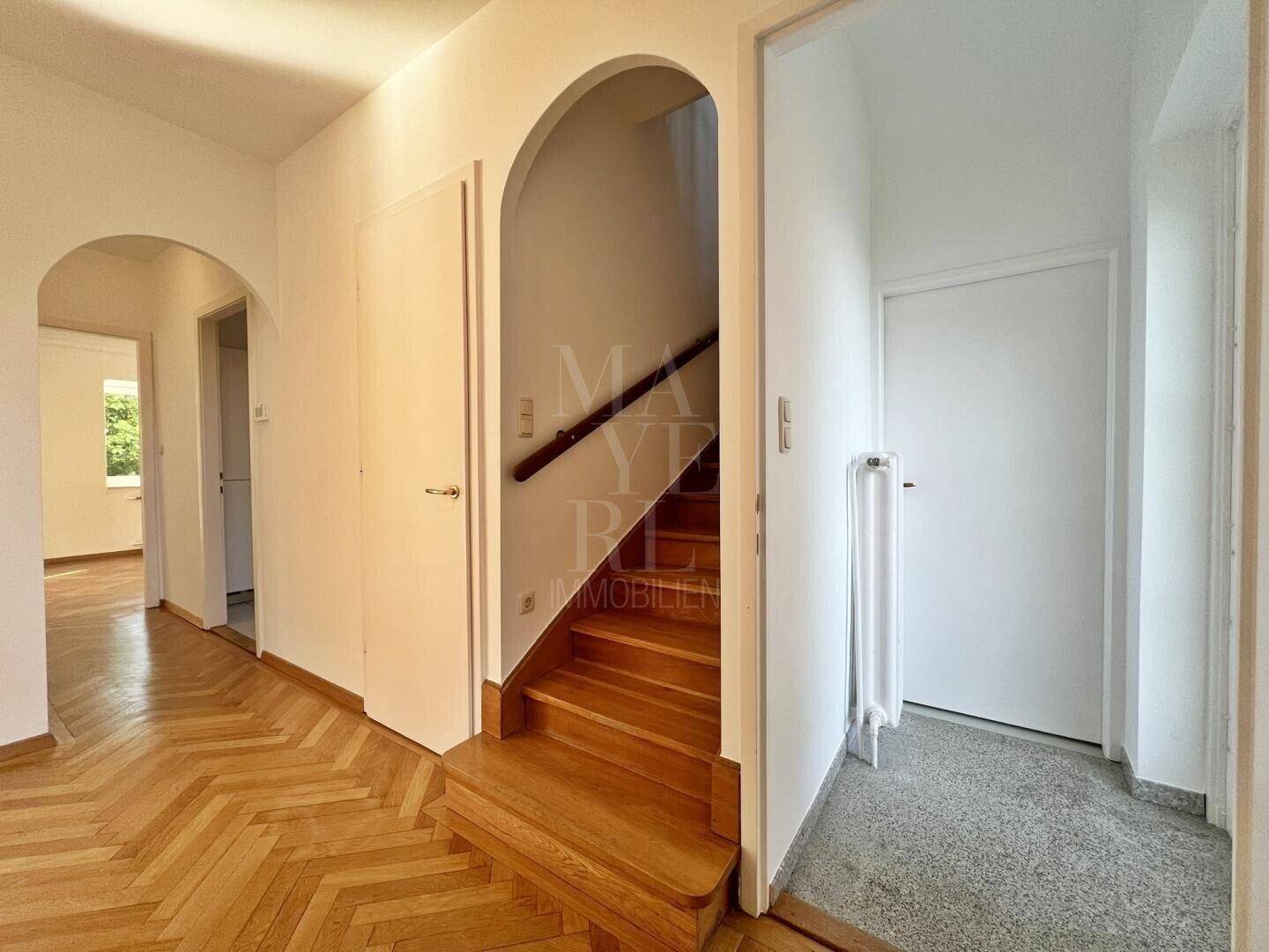 Geräumiger Flur mit Fischgrätparkett und einer Holztreppe, die in die oberen Stockwerke führt.
