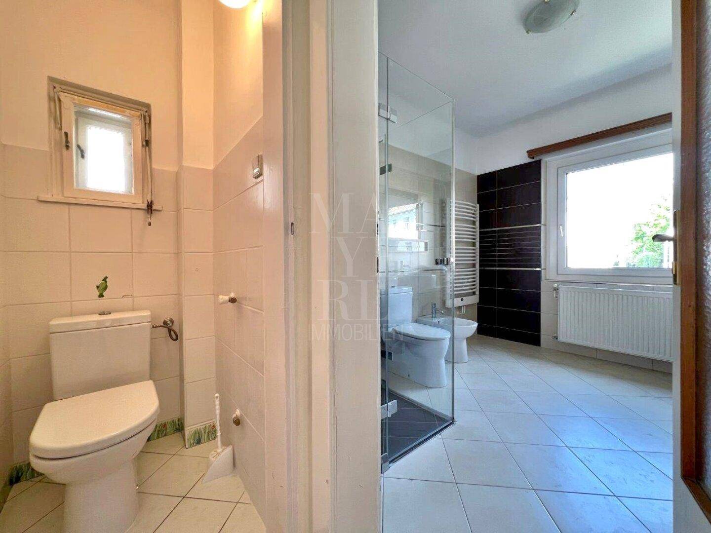 Modernisiertes Badezimmer mit Duschkabine, WC, Bidet und Fenster, das für Belüftung sorgt.