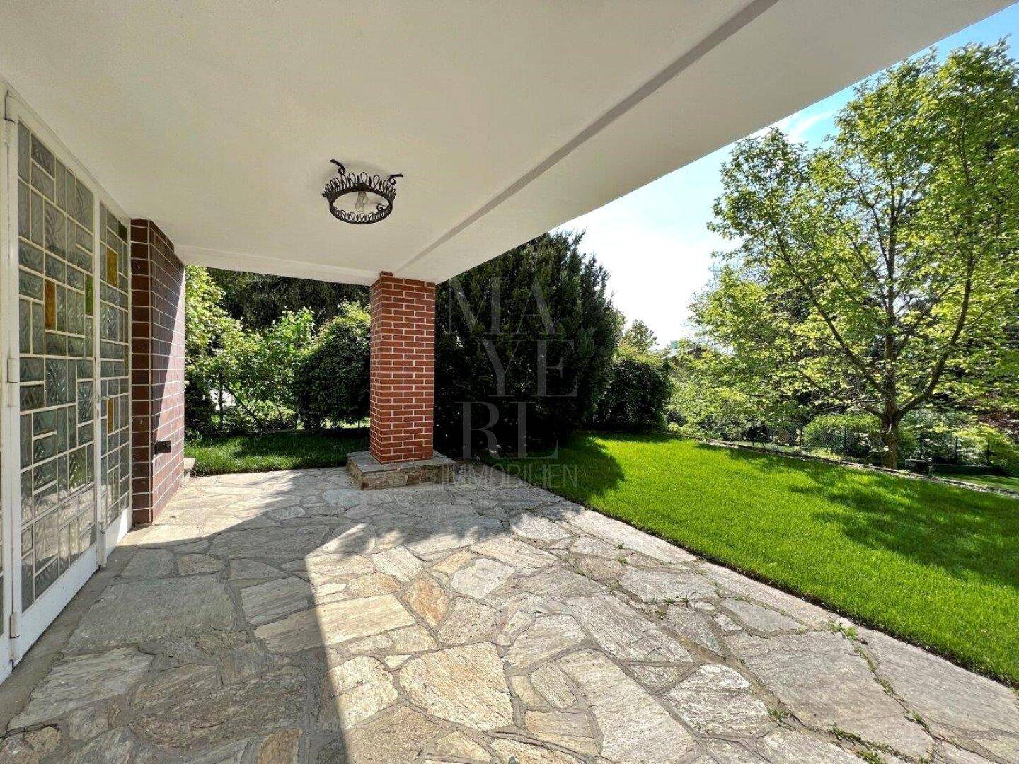 Überdachte Steinterrasse mit Blick auf den großen Garten, ideal für entspannte Stunden im Freien.
