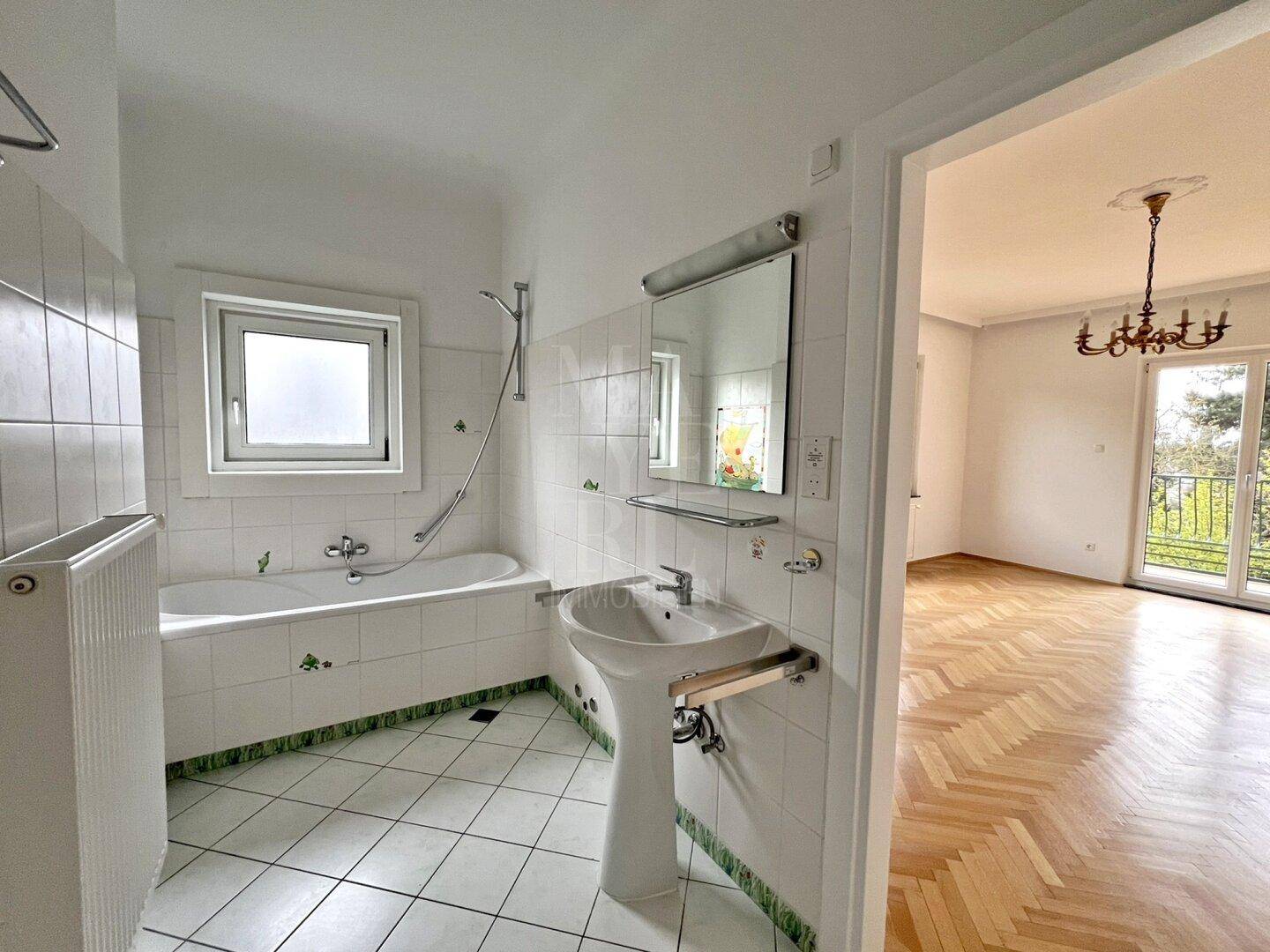 Helles Badezimmer mit Badewanne, Waschbecken und Fenster, das viel Tageslicht hereinlässt.