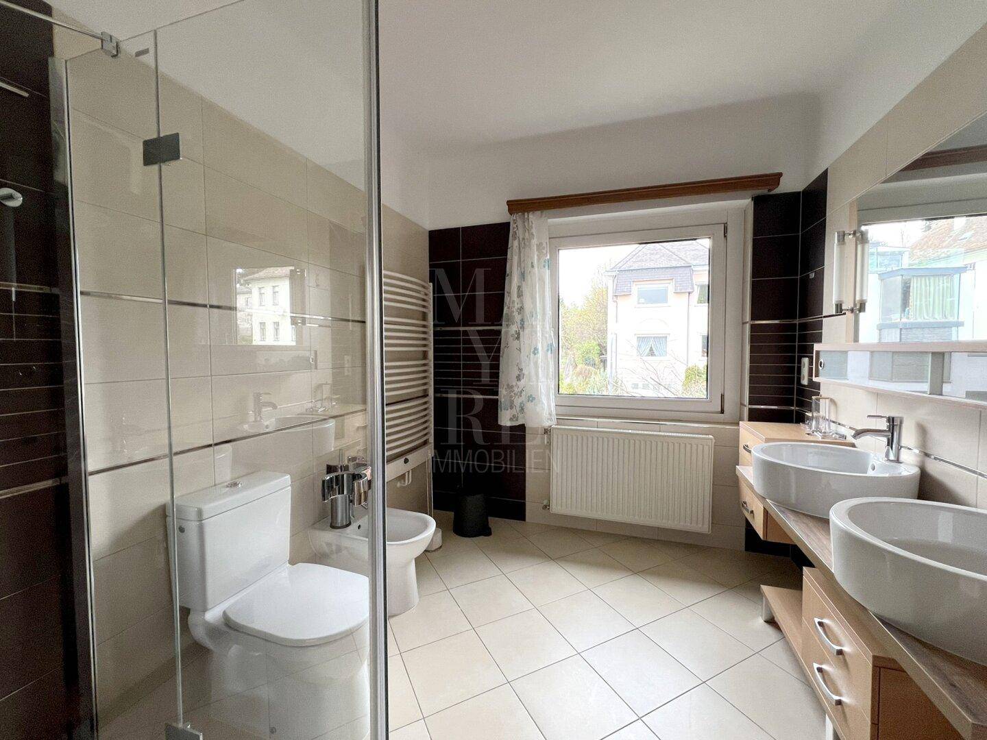 Modernes Badezimmer mit Doppelwaschbecken, Duschkabine, WC und Bidet, ausgestattet mit einem Fenster.