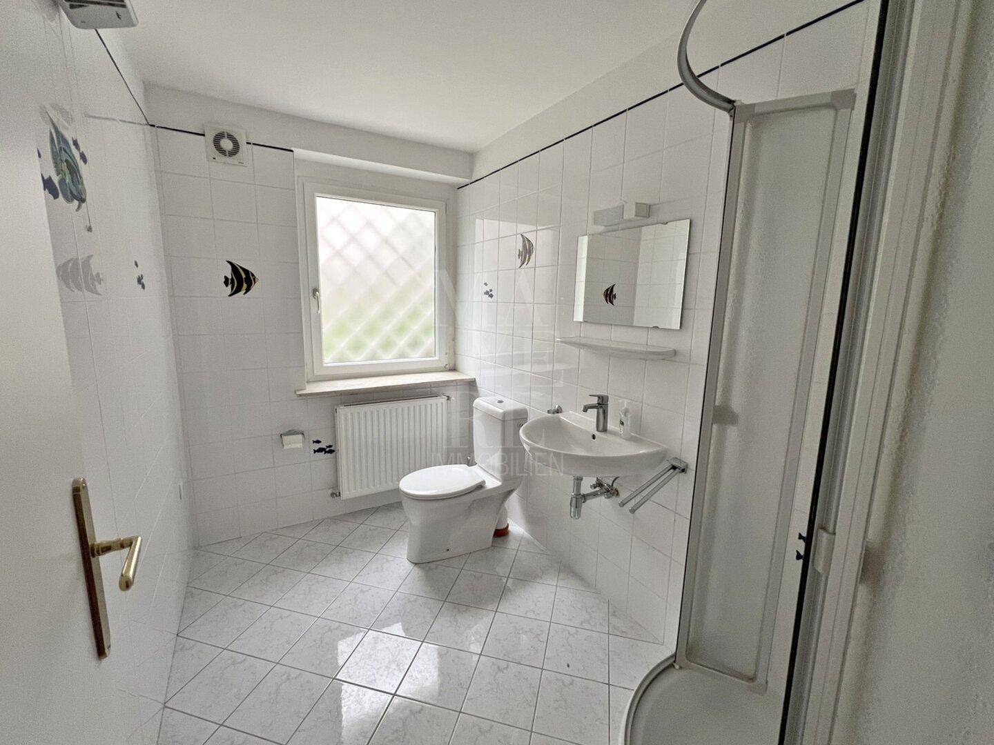 Helles Badezimmer mit Dusche, WC, Waschbecken und Fenster, dekoriert mit Fischmotiven.