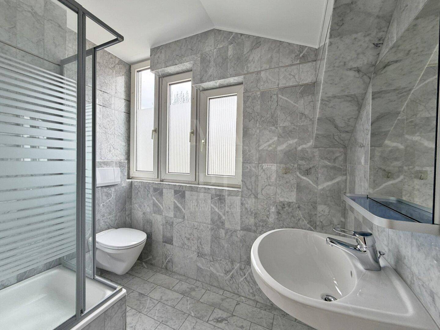 Modernes Badezimmer mit grauen Marmorfliesen, Duschkabine, Toilette und Waschbecken.
