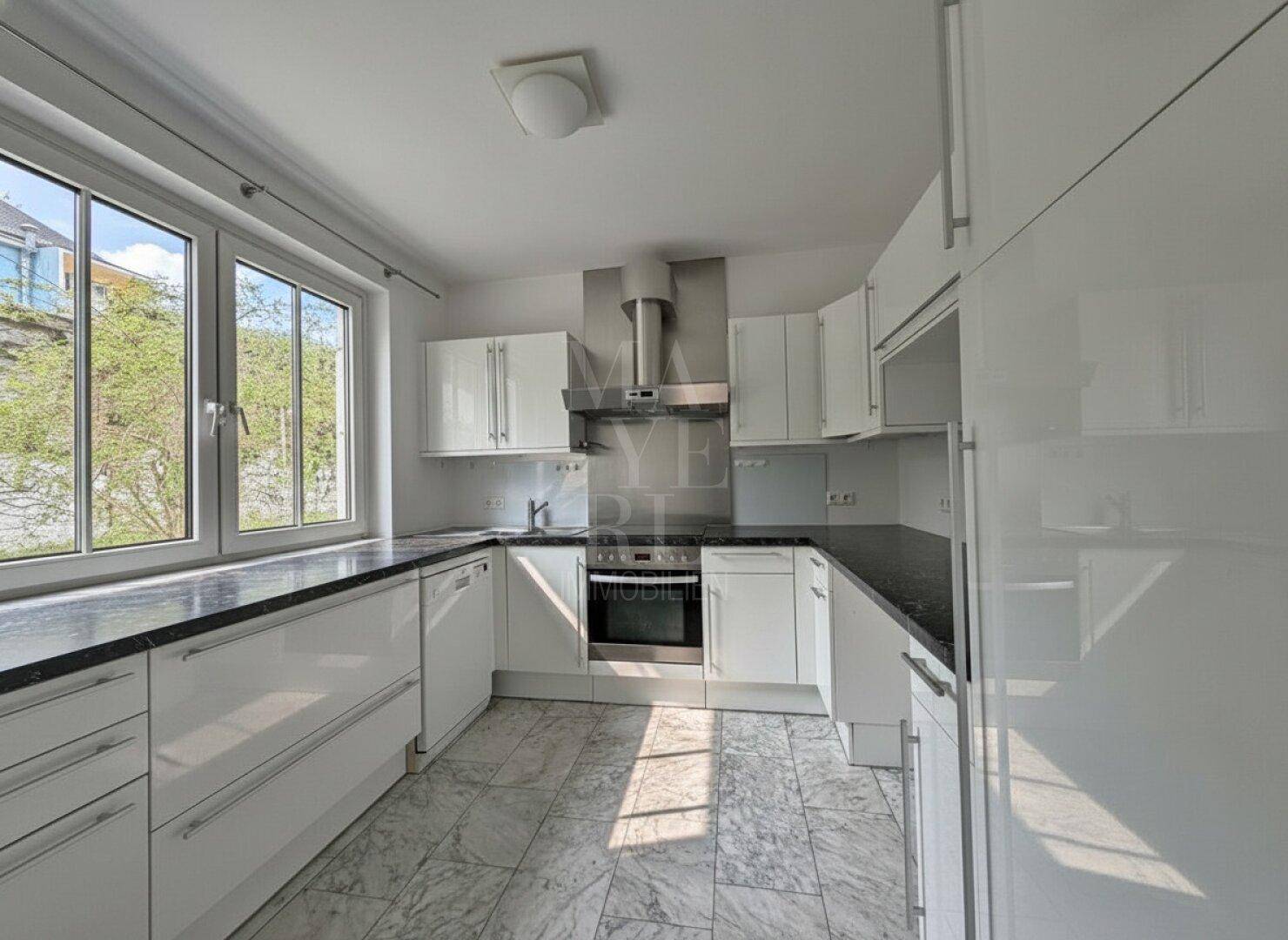 Moderne Küche mit weißen Hochglanzschränken, dunklen Arbeitsplatten und großem Fenster.