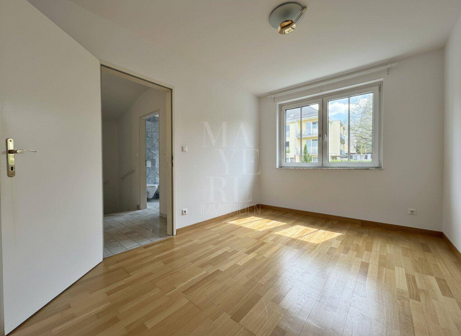 Schlafzimmer mit hellem Holzfußboden und Fenster, das Tageslicht in den Raum lässt.