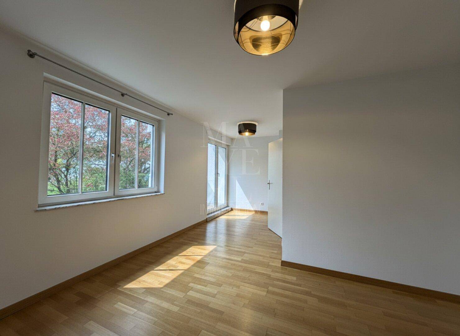 Helles Schlafzimmer mit Holzparkett, großem Fenster und Zugang zu einem Balkon.