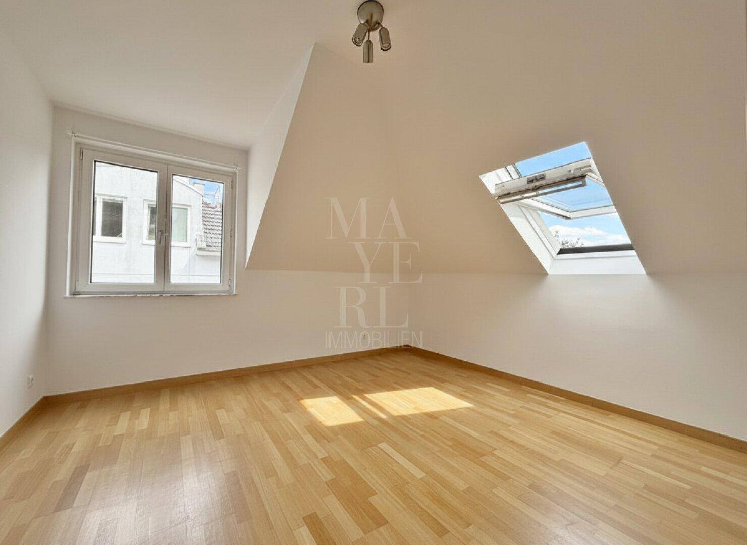 Helles Dachzimmer mit Holzfußboden, Dachschräge und einem zusätzlichen Dachfenster.