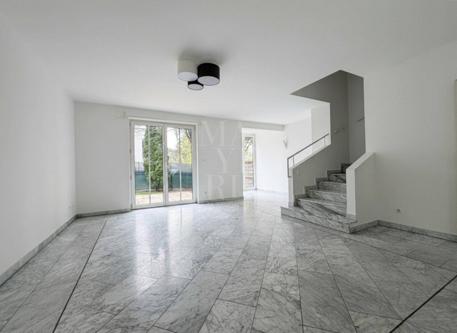 Geräumiges, helles Wohnzimmer mit Marmorfliesenboden, Treppe und Zugang zum Garten.