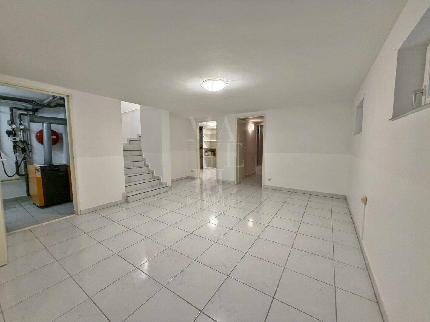 Geräumiger Kellerraum mit Fliesenboden und Zugang zu einem Technikraum und Treppenhaus.
