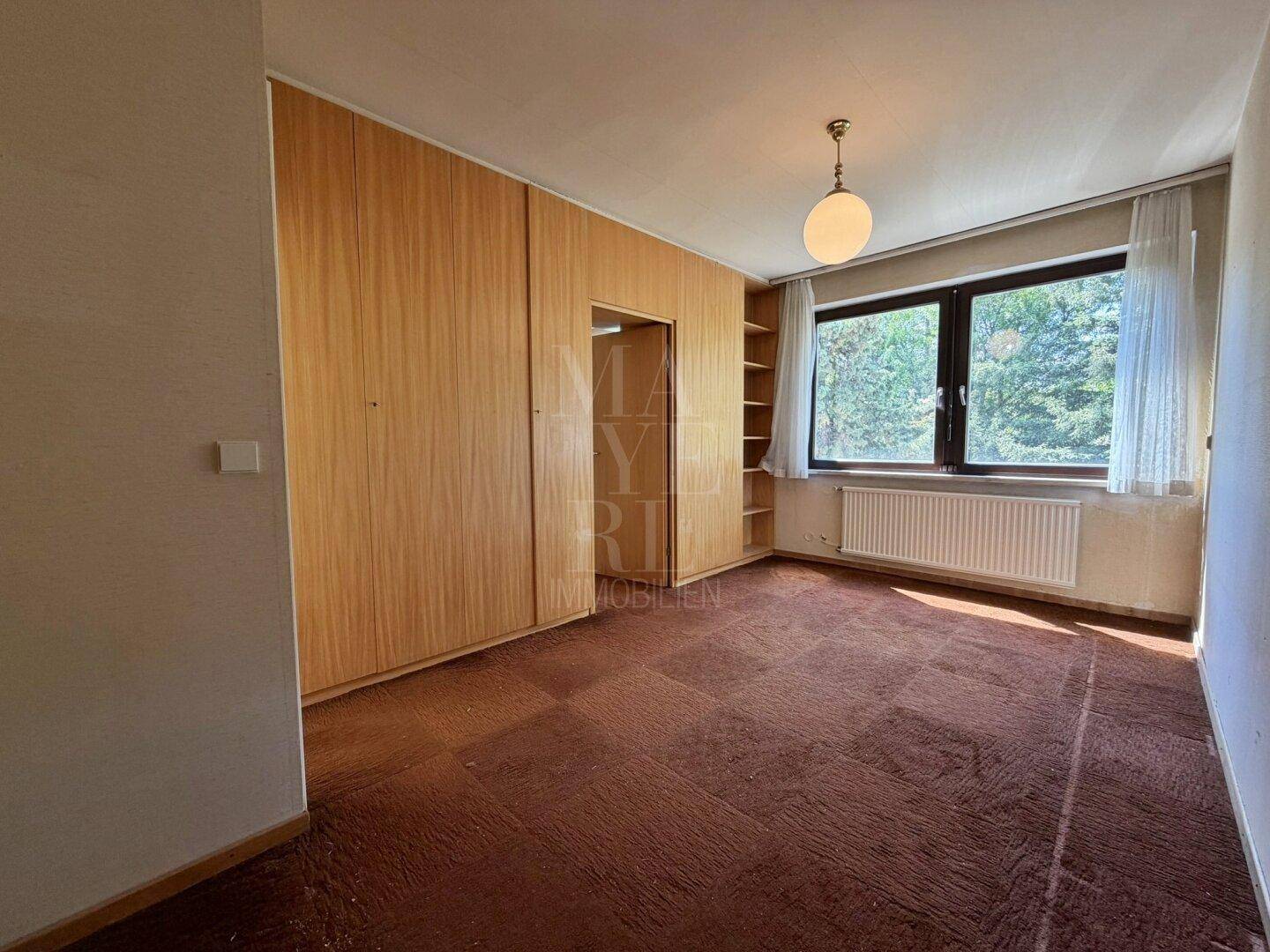 Schlafzimmer mit Teppichboden, Einbauschränken und großem Fenster mit Grünblick.