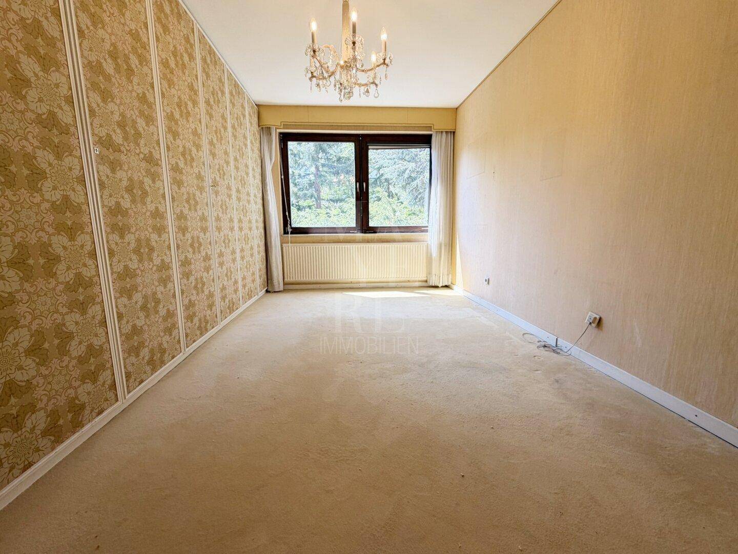 Helles Schlafzimmer mit Teppichboden, gemusterter Tapete und großem Fenster.