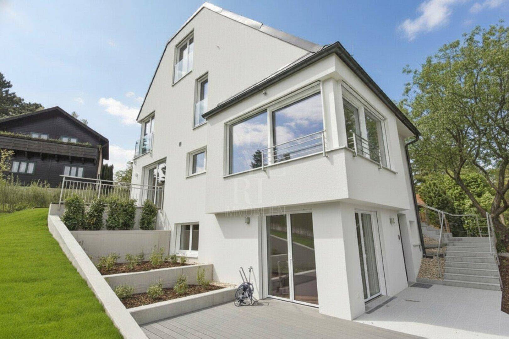 Ansicht des modernen Hauses von der Seite mit gestuftem Garten, Außentreppe und Holzterrasse.