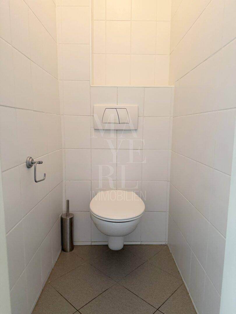 Separates WC mit wandhängender Toilette und weißen Fliesen, sauber und funktional.