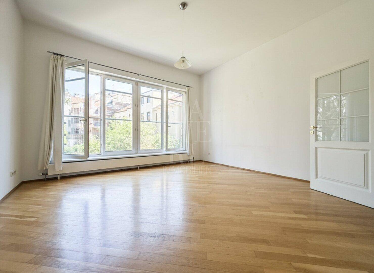 Helles Wohnzimmer mit großen Fenstern und glänzendem Parkettboden, bereit zur individuellen Gestaltung.