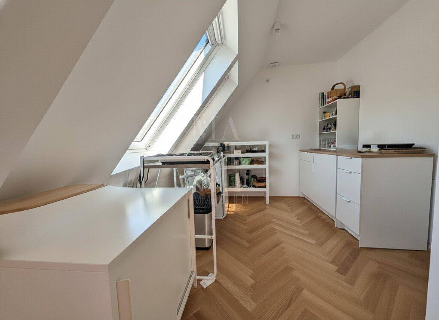 Dachgeschossküche mit Schrägdach, Dachfenster und einfacher Küchenzeile.