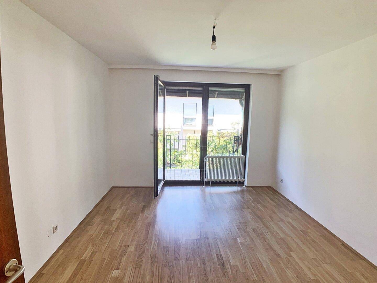 Helles Schlafzimmer mit Parkettboden und Balkonzugang, bietet einen angenehmen Ausblick.