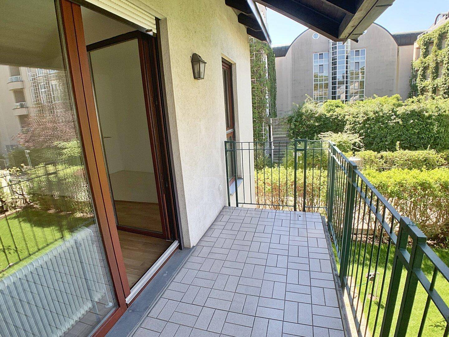 Kleiner Balkon mit Fliesenboden und Blick auf den Garten und die umliegenden Gebäude.