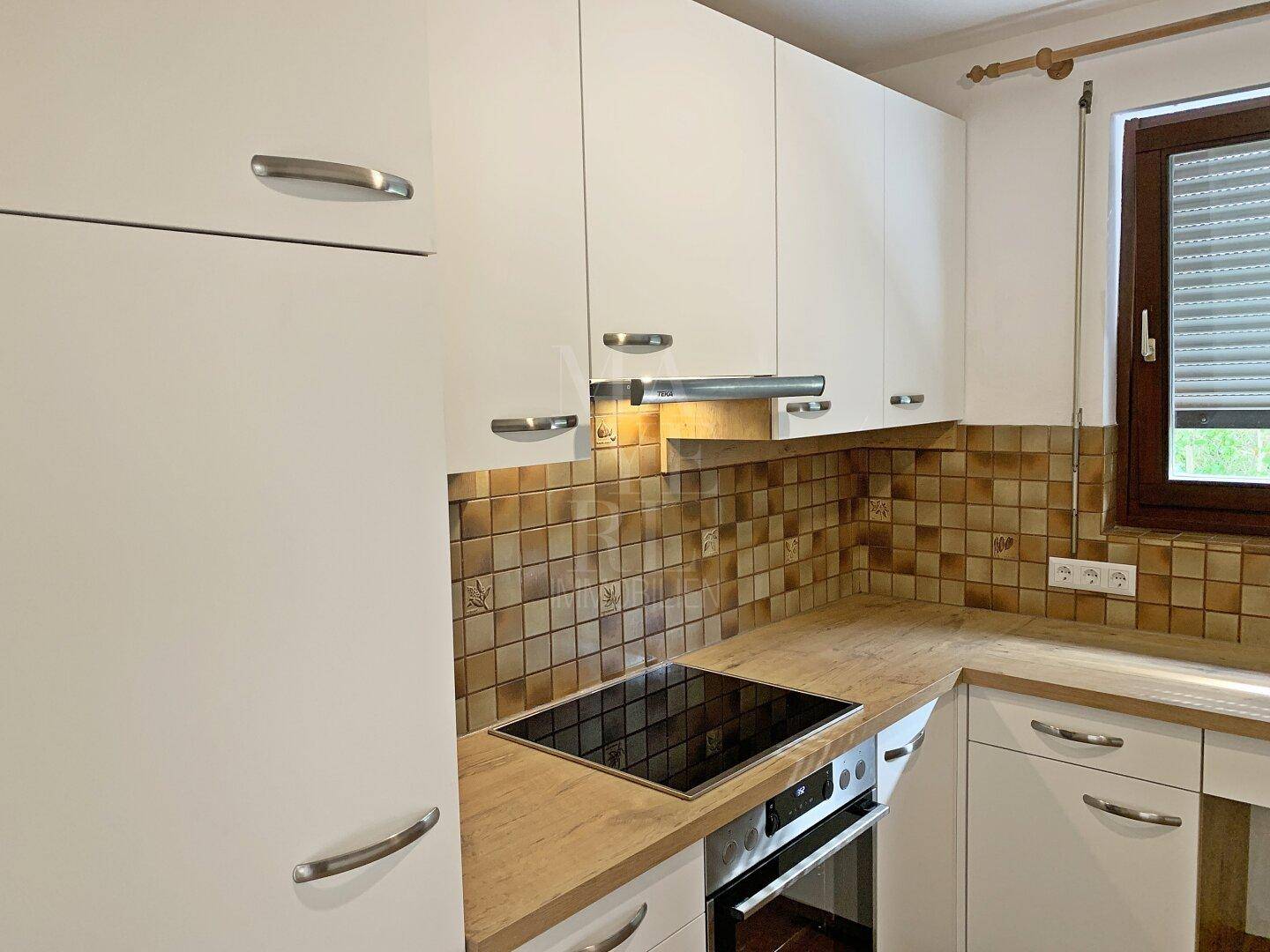 Einbauküche mit Induktionskochfeld, Backofen und weißen Schränken, ergänzt durch Holz-Arbeitsplatten.