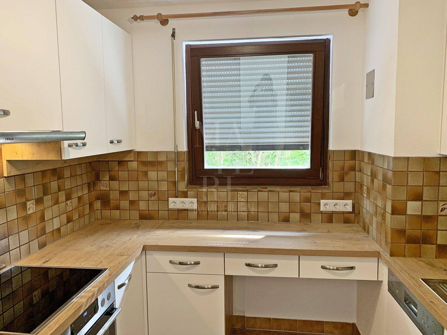 Funktionale Küche mit hellen Schränken, Holz-Arbeitsplatte und braunen Fliesen als Spritzschutz.