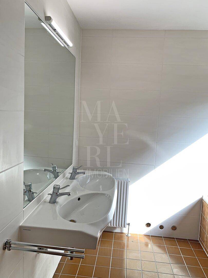 Badezimmer mit Doppelwaschbecken und großem Spiegel, gefliest in hellen und braunen Tönen.