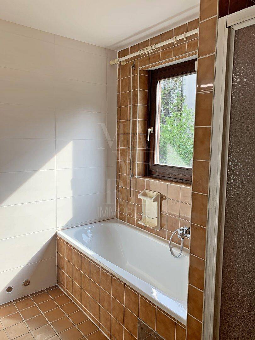 Badezimmer mit Badewanne und Fenster, gefliest in braunen und weißen Farbtönen, gut belichtet.