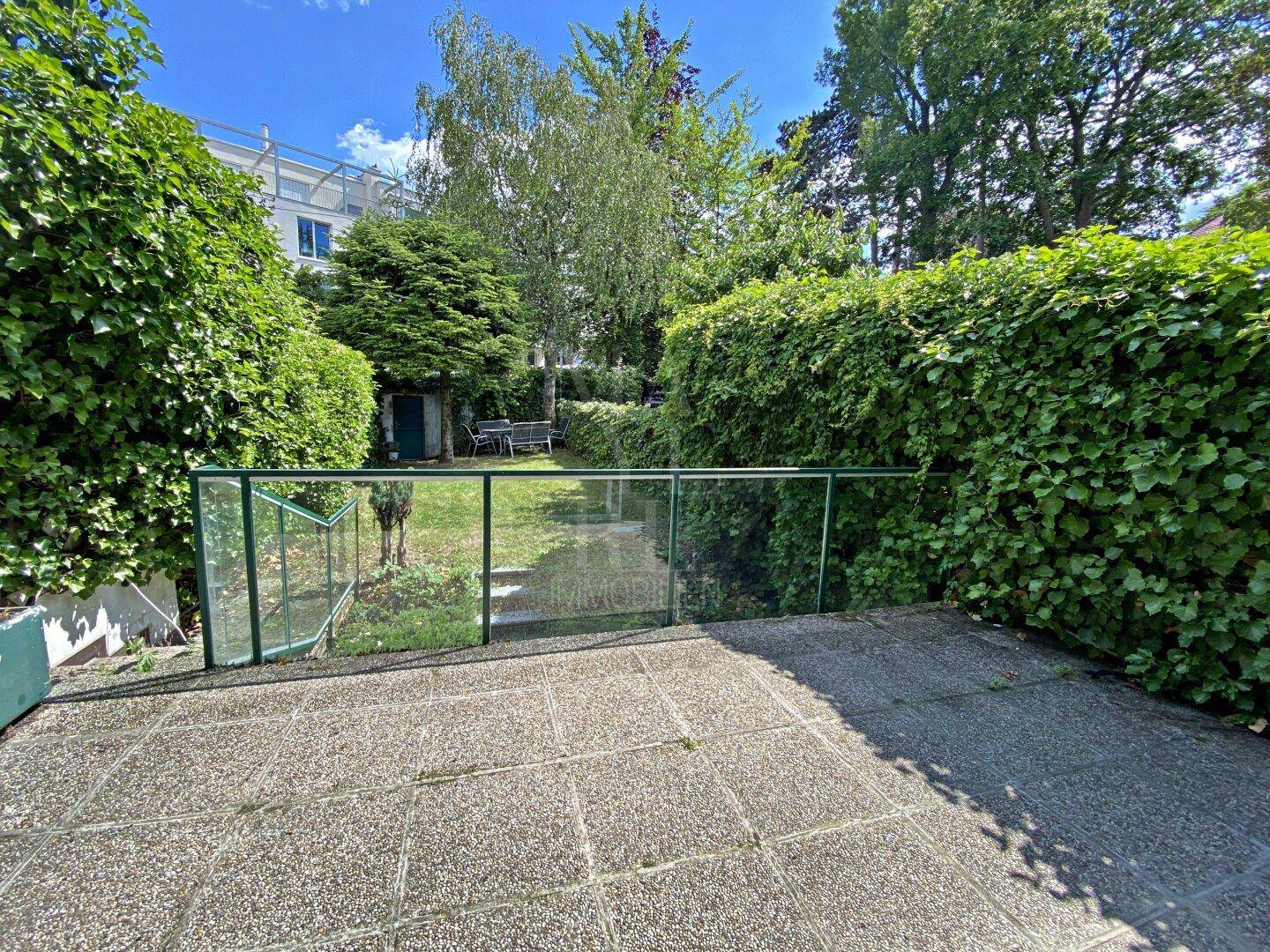 Gepflasterte Terrasse mit Glasgeländer und Blick auf den gepflegten, grünen Gartenbereich.