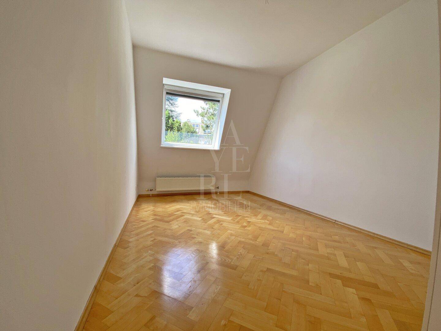Helles Schlafzimmer mit Fischgrätparkett, Dachschräge und einem Dachfenster für Tageslicht.